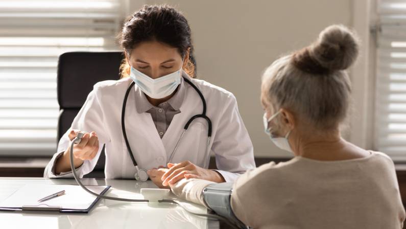 female doctor wearing face mask measuring checking old woman blood pressure